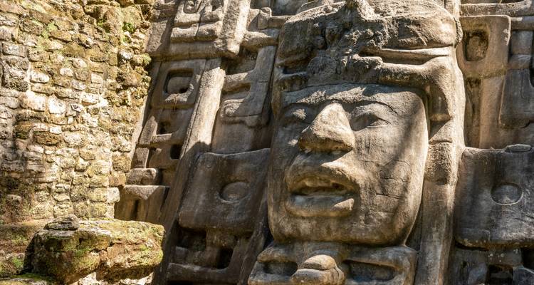 Close-up of intricately carved Mayan stone mask on a temple facade in the jungle.