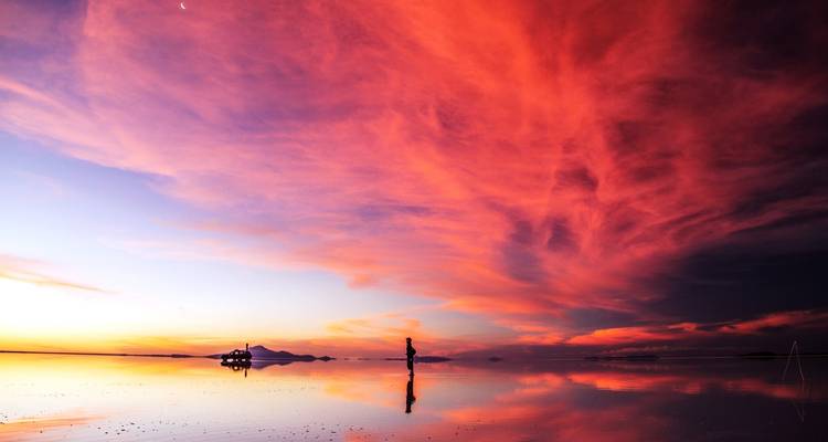 Persoon die staat op reflecterende zoutvlakten tijdens zonsondergang met levendige wolken