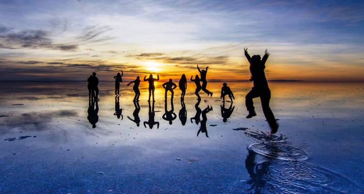 Silhouetten van mensen die springen en poseren op reflecterende zoutvlaktes tijdens zonsondergang