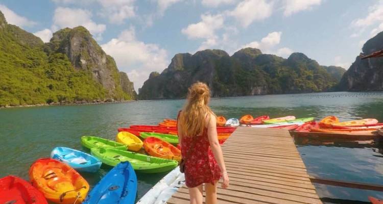 Woman walking toward colorful kayaks by a dock, with limestone cliffs in the background.