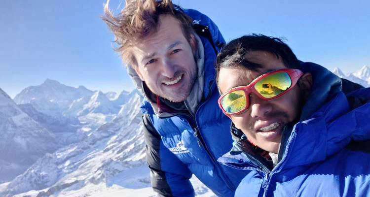 Twee bergbeklimmers poseren voor een foto, met een besneeuwde Himalaya-achtergrond.
