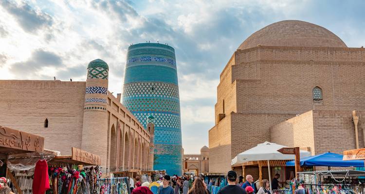 A bustling market street with vendors and historic buildings, including a large minaret.