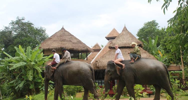 Menschen, die auf Elefanten reiten, in der Nähe traditioneller strohgedeckter Gebäude.