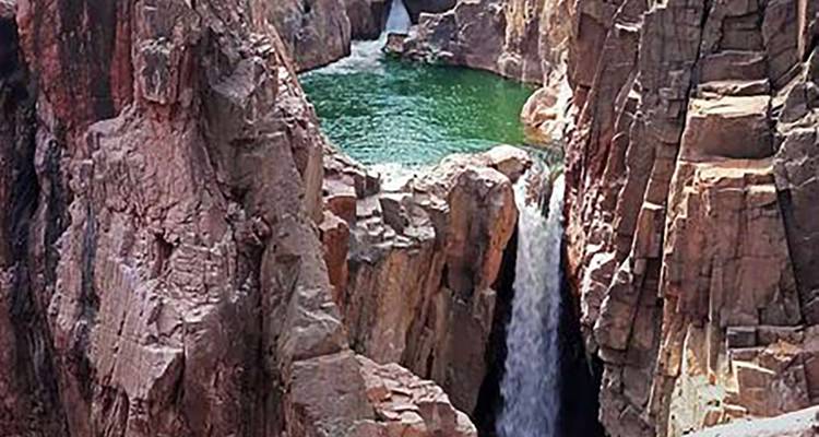 Wasserfall, der in eine felsige Schlucht mit üppiger Umgebung stürzt.