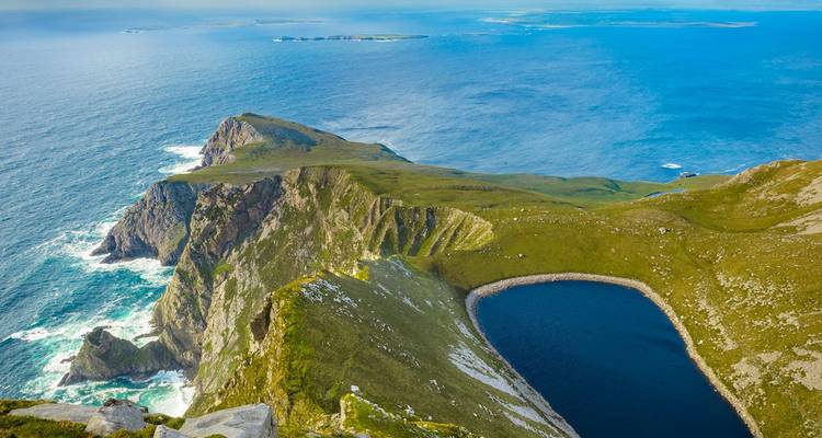Spectaculaire kliffrand van Achill Island met een diepblauw meer en Atlantische golven eronder.