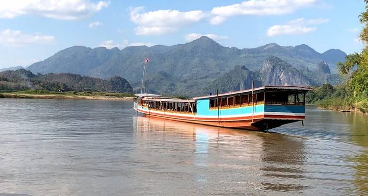 Langes Boot auf einem ruhigen Fluss mit Bergen im Hintergrund.