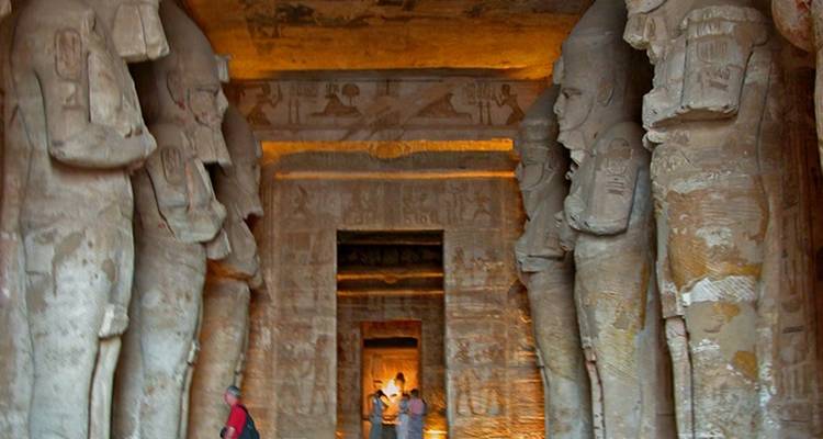 Intérieur d'un temple taillé dans la roche avec des statues bordant un corridor.