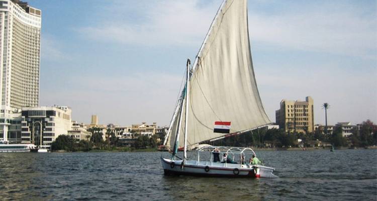 Voilier sur une rivière avec des bâtiments urbains en arrière-plan.