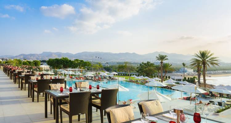 Freiluft-Restaurantterrasse mit Blick auf einen Pool und die Küstenlinie mit Bergaussichten.