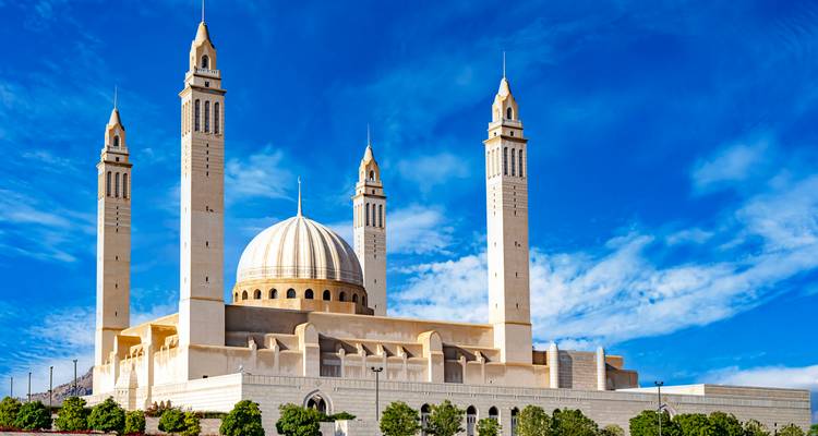 Die Sultan-Qabus-Moschee mit vier schlanken Minaretten und einer großen weißen Kuppel unter blauem Himmel.