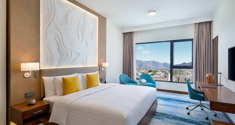 Modernes Hotelzimmer mit Bergblick aus dem Fenster, blauen Stühlen und abstrakter Kopfendkunst.