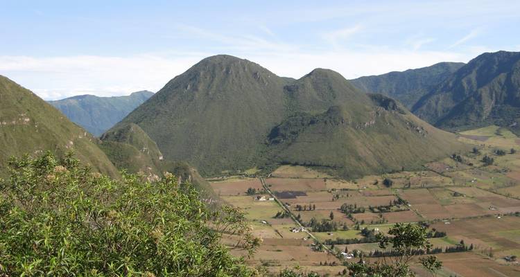 Broad panorama of steep green volcanic cones towering over fertile agricultural fields.