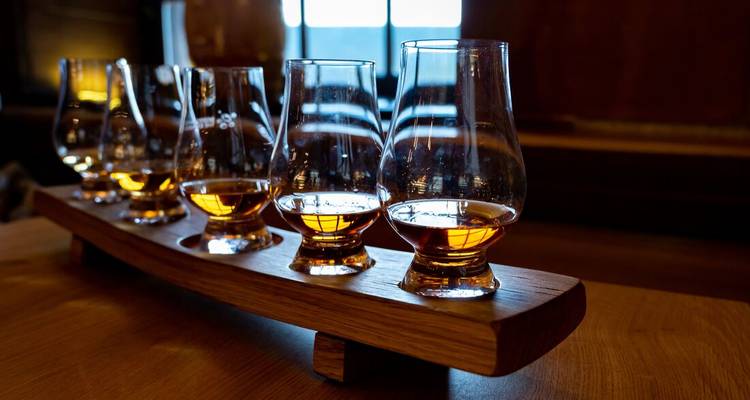 Des verres de whisky alignés sur un plateau en bois.