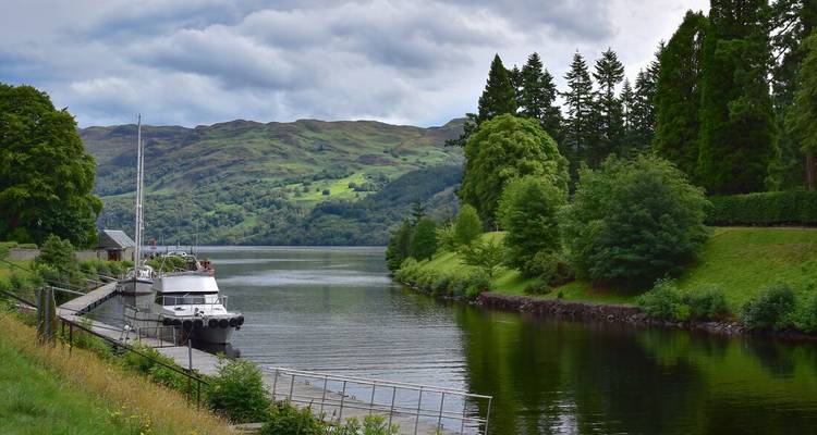 Bateau amarré sur une rivière calme bordée de collines vertes.
