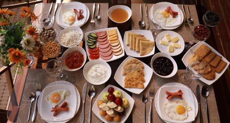 Ein Tisch voller Teller und Schüsseln mit verschiedenen Frühstücksgerichten wie Eiern, Würstchen, Gemüse, Obst und Brot.
