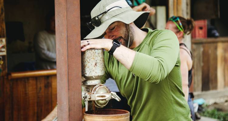 Personne préparant du café avec un moulin manuel, en extérieur.