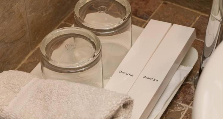 Tablett mit Zahnpflegesets, Glas und Handtüchern auf einer Badezimmerablage.