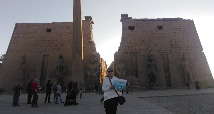 Eine Person mit einem Schild vor antiken Ruinen bei Sonnenuntergang.