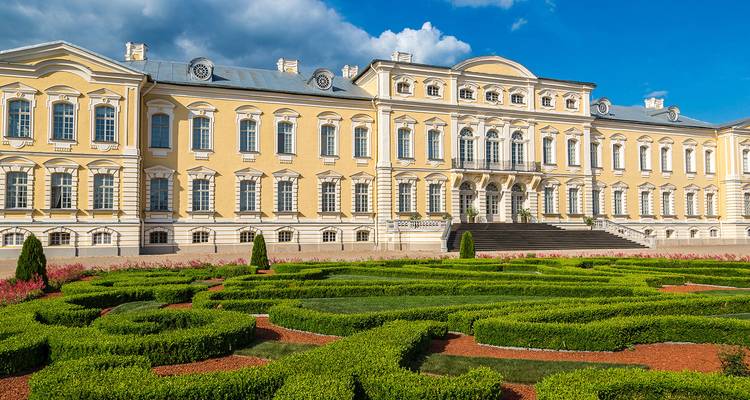 Elegant Rundale Palace fronted by manicured baroque gardens under a deep blue sky.