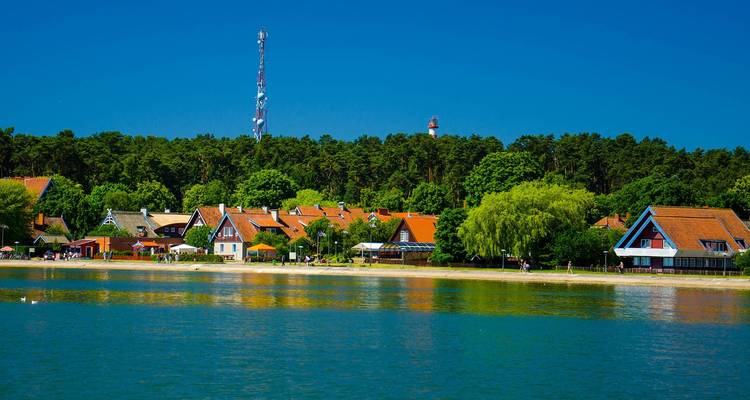 Charming waterfront cottages with red roofs reflect on the calm lagoon at Nida.