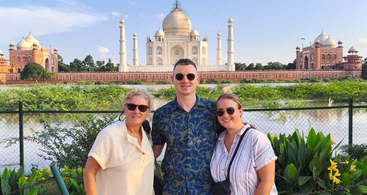 Tres viajeros posan sonriendo frente al Taj Mahal en un día de cielo azul brillante