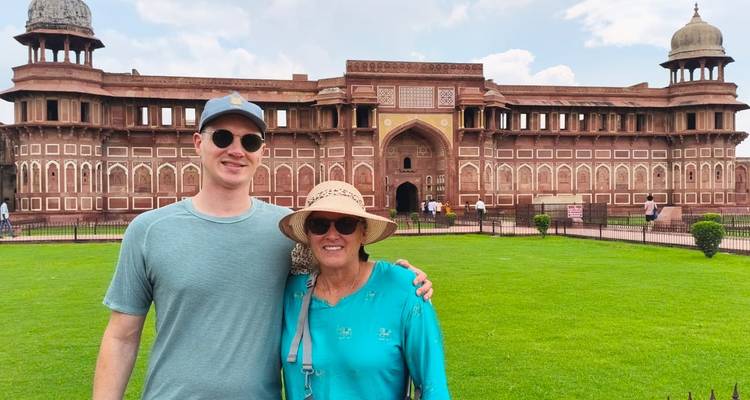 Dos viajeros están parados frente a las murallas de arenisca roja del Fuerte de Agra rodeados de céspedes verdes