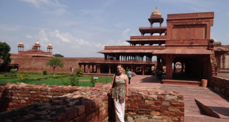 A visitor stands near the terraced pavilions of Fatehpur Sikri under bright skies