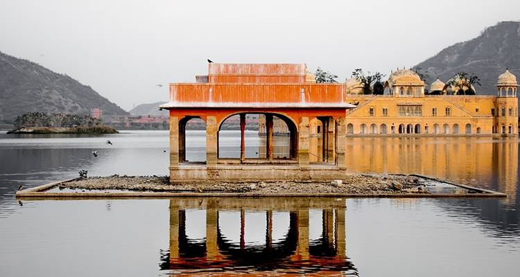 Een sierlijke structuur weerspiegeld op een serene meer met een heuvelachtige achtergrond.