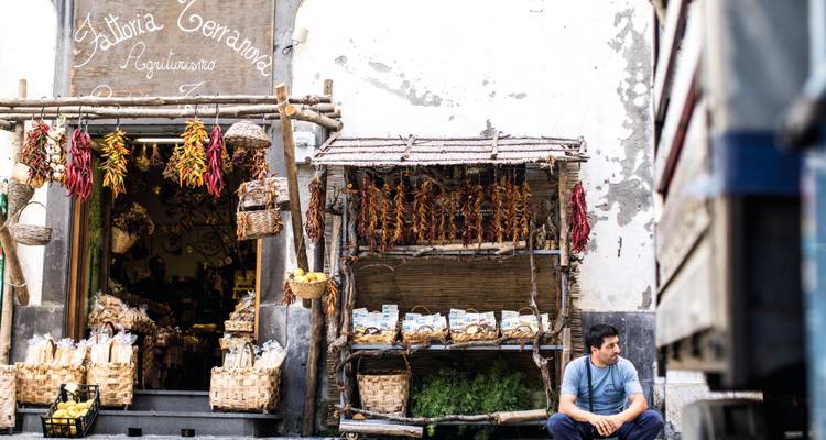 Devanture commerciale locale ornée de piments séchés suspendus et de produits; homme assis dehors se reposant.