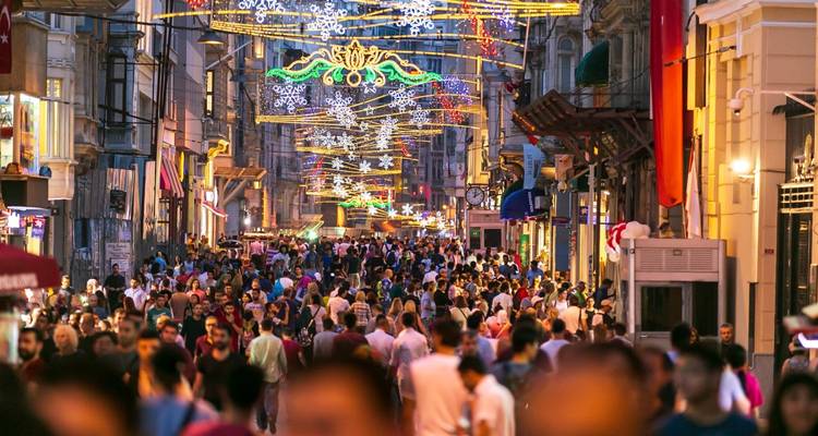 A bustling pedestrian street packed with evening shoppers beneath festive overhead lights.