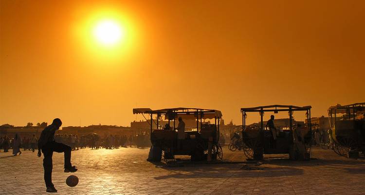 Silhouette einer Person, die bei Sonnenuntergang auf einem Marktplatz Fußball spielt