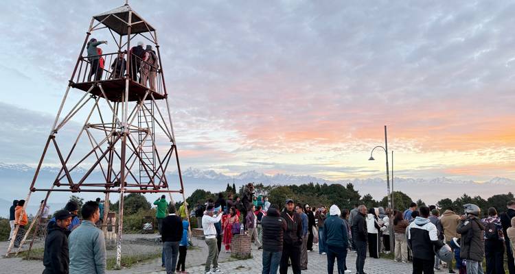People gathered near a tower with mountains in the background.