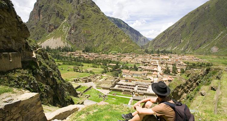 Een persoon die zit en uitkijkt over de archeologische site met bergen op de achtergrond.