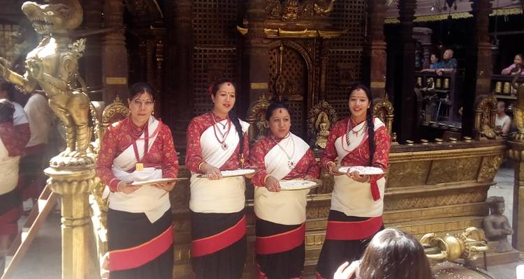 Vier Frauen in traditioneller Kleidung, die Tabletts halten.