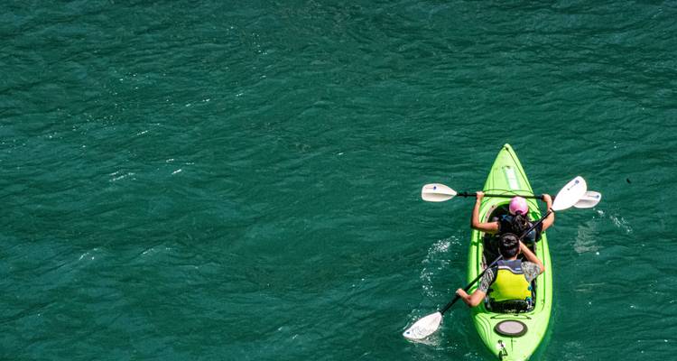 Vue de dessus de deux personnes pagayant dans un kayak vert vif sur une eau émeraude.