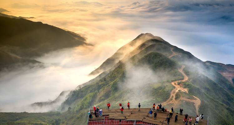 Terrasse d'observation en montagne dominant une mer de nuages au lever du soleil avec de nombreux visiteurs prenant des photos