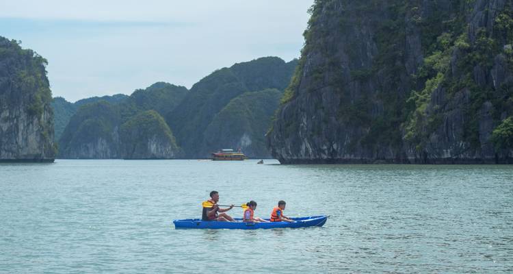 Une famille pagaie dans un kayak bleu sur des eaux émeraude calmes entourée d'îles calcaires imposantes