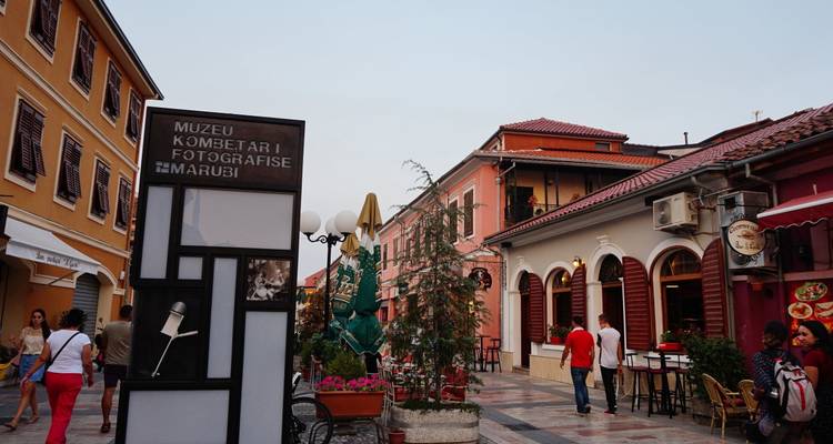 Straßenansicht mit Schildern von Kulturmuseen, geschäftigen Menschen und Cafés in einer historischen Stadt.