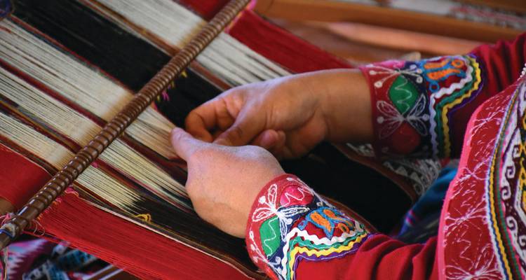 Gros plan des mains d'artisan tissant des textiles andins colorés sur un métier à tisser traditionnel.