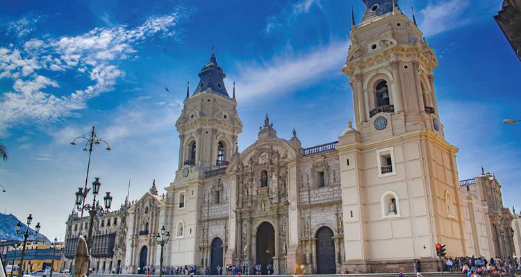 La façade ornée et les deux clochers jumeaux de la Cathédrale de Lima s'élèvent contre un ciel bleu éclatant alors que les visiteurs se rassemblent en dessous.