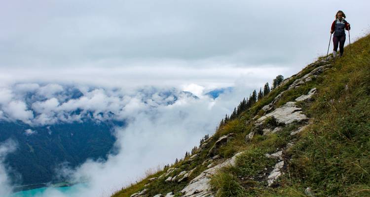 Excursionista con bastones de trekking desciende por la ladera de la montaña brumosa sobre la capa de nubes