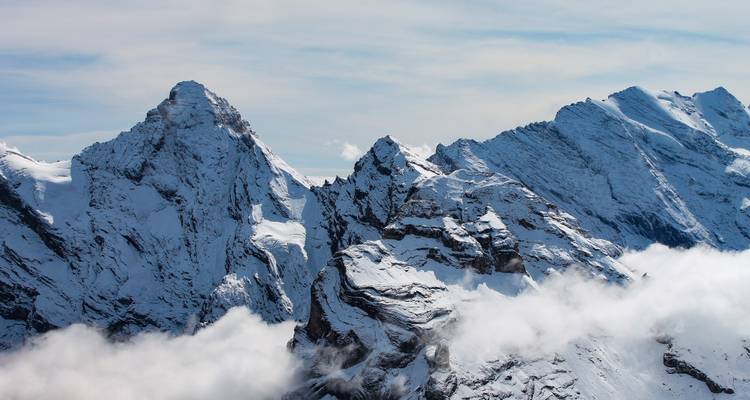 Picos alpinos dentados cubiertos de nieve sobresaliendo por encima de la capa de nubes bajas