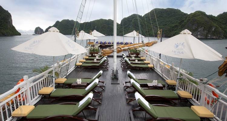 Deck eines Bootes mit Liegestühlen und Sonnenschirmen mit Blick auf Felsformationen.