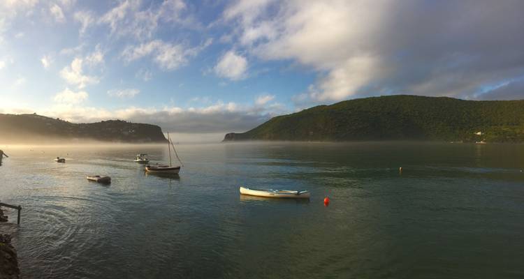 Calm water bay with boats and lush hills.