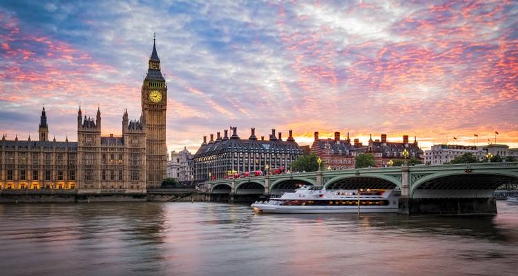 Big Ben et les Chambres du Parlement se reflétant dans la Tamise lors d'un coucher de soleil coloré avec un bateau passant sous le pont de Westminster.