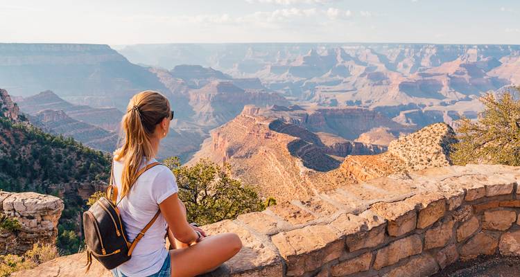 Een persoon zittend op een muur, genietend van het uitzicht over een uitgestrekte canyon.