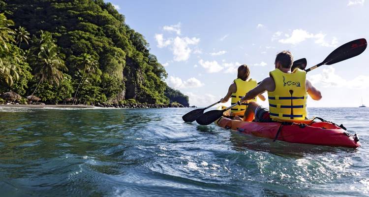 Couple faisant du kayak sur un océan calme avec en arrière-plan une végétation luxuriante.