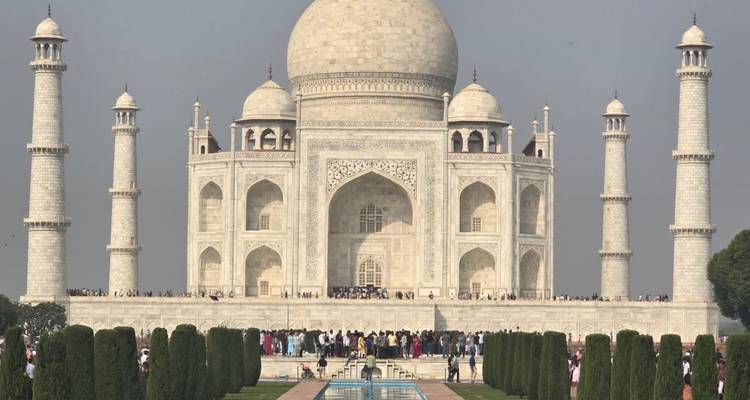 Iconisch frontaal uitzicht van de Taj Mahal met reflectievijver en drukte van bezoekers op een mistige dag.