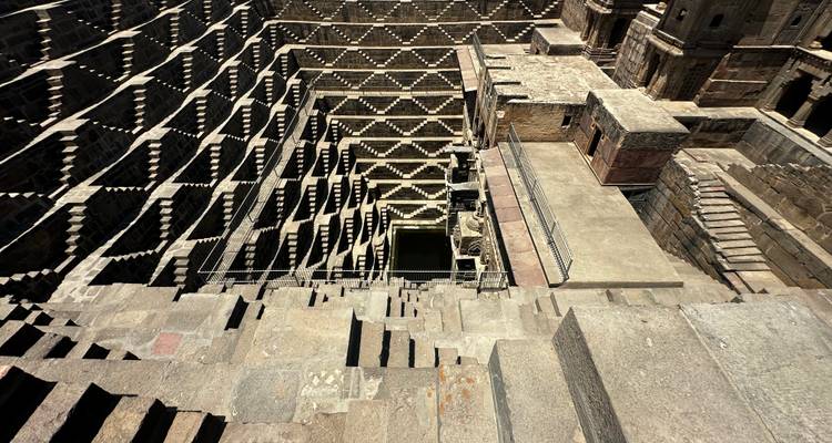 Duizelingwekkend uitzicht naar beneden over de geometrische trappen van Chand Baori stepwell in Rajasthan onder de felle zon.