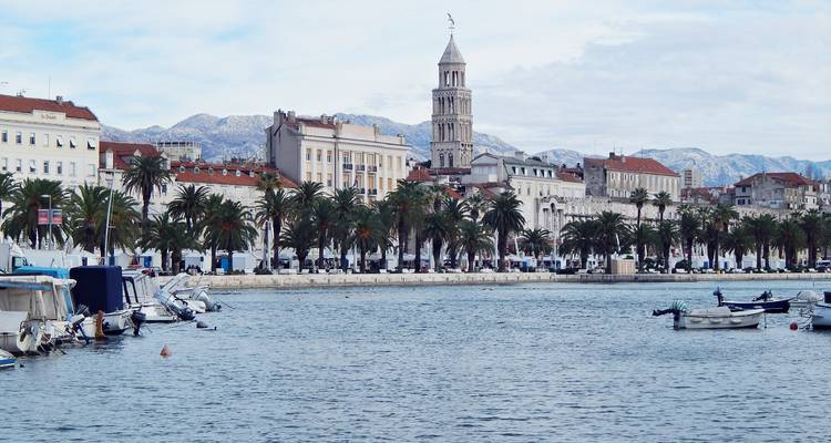 Geteilte Hafenpromenade mit Palmenreihen, Booten und dem Kathedralenturm mit Bergen im Hintergrund